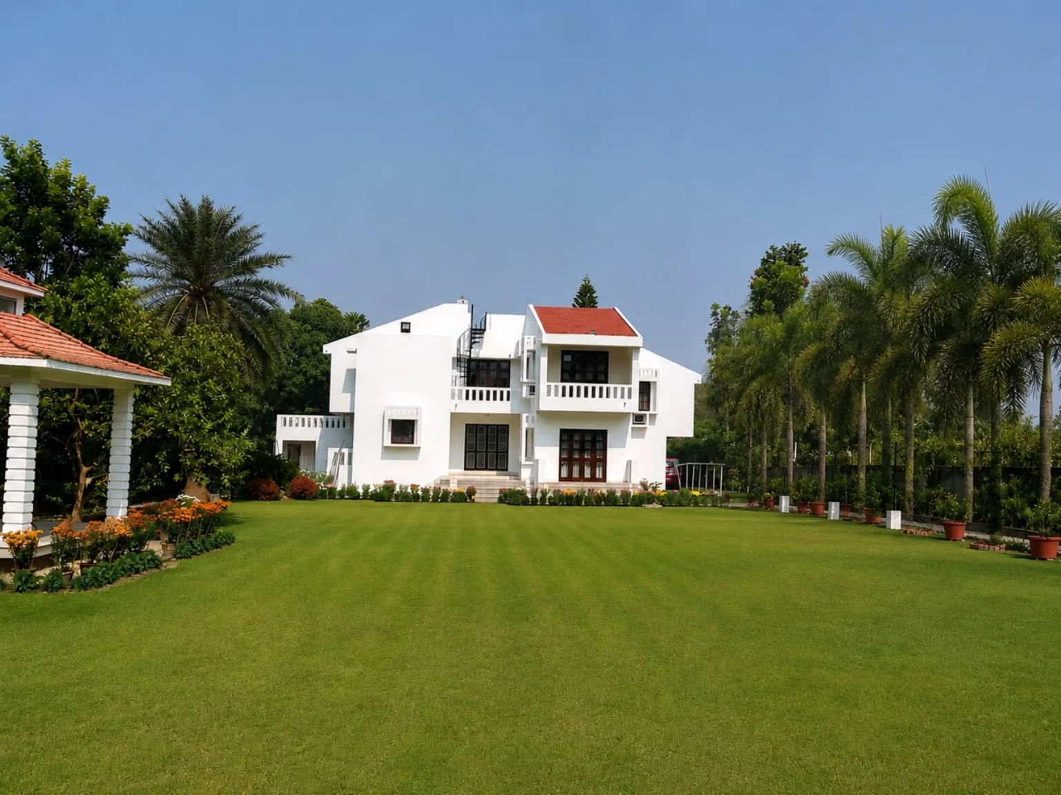 An expansive lawn leads toward a white building, with palms along the boundary.