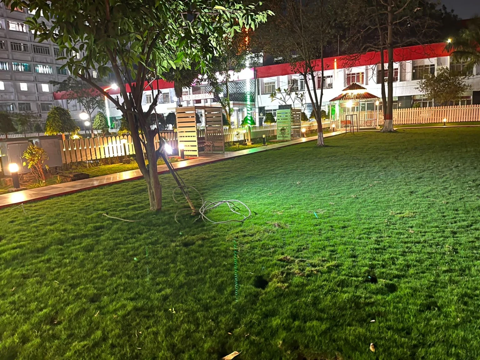 A green lawn with trees, garden structures and illuminated boundaries.