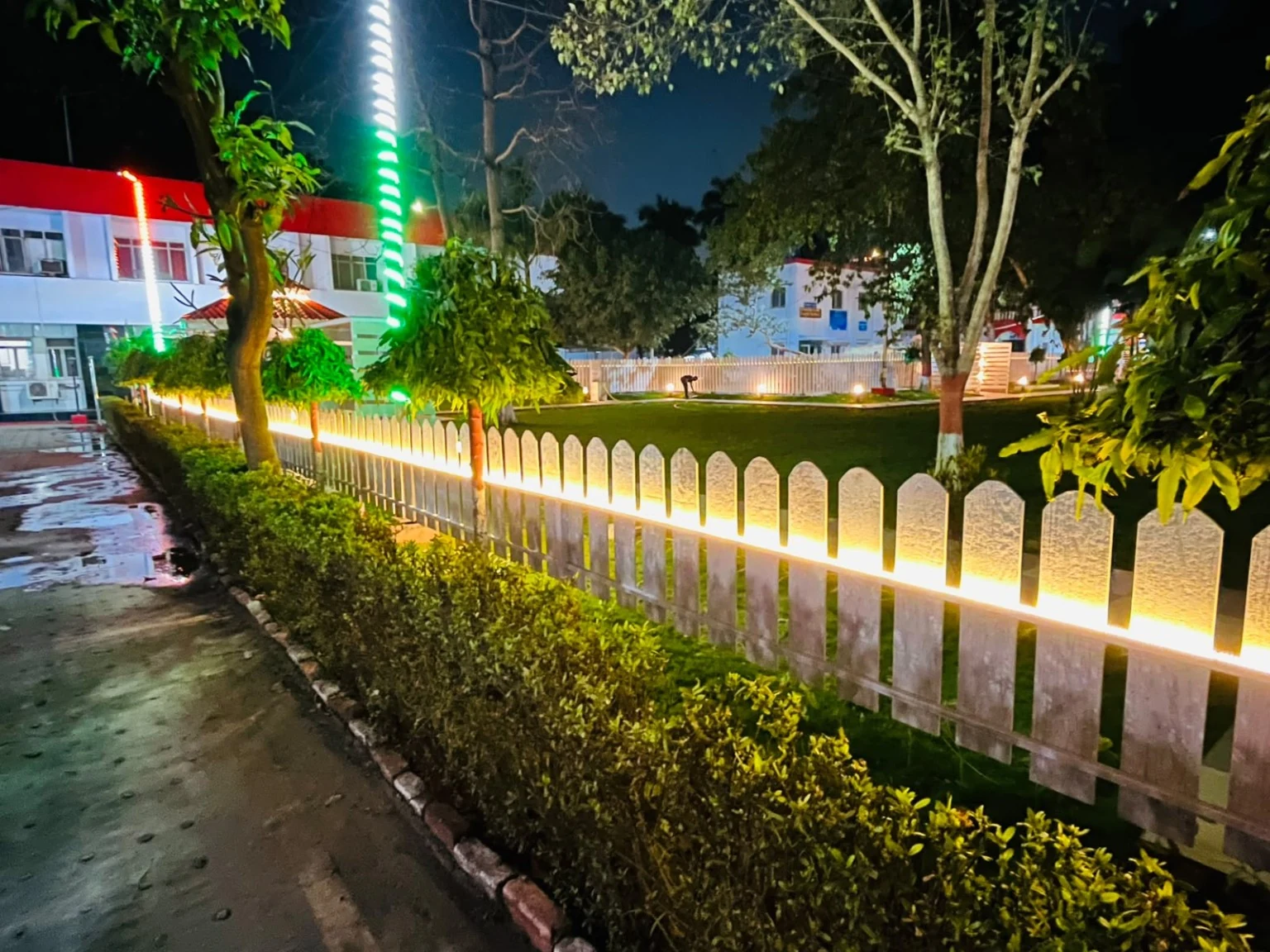 A planted roadside boundary with white fencing and warm lighting.