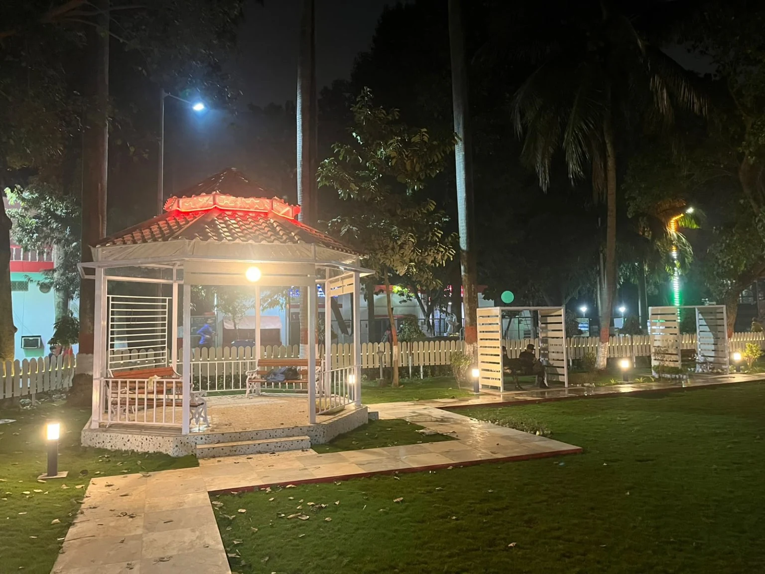 An illuminated gazebo set within a lawn and bordered by a garden path.